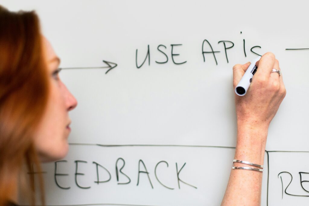 pexels-photo-3861943-3861943 A woman writes 'Use APIs' on a whiteboard, focusing on software planning and strategy.