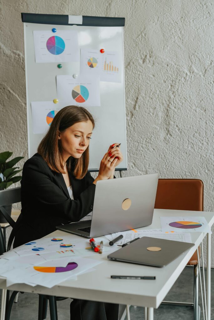 pexels-photo-8145346-8145346 Focused businesswoman working on laptop at desk with charts and graphs in a modern office setting.
